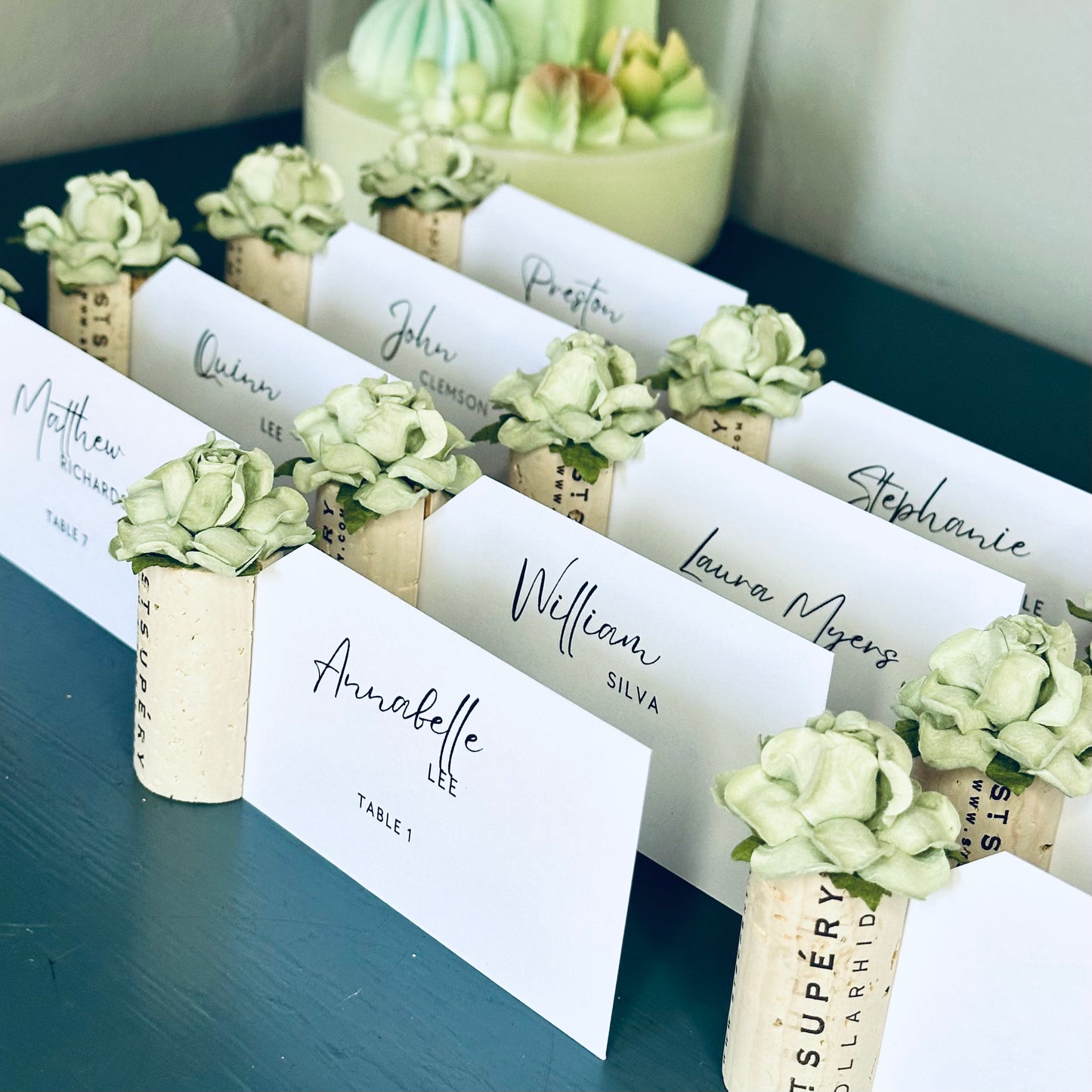 Place cards with succulent flowers on wine corks, arranged on a blue surface.