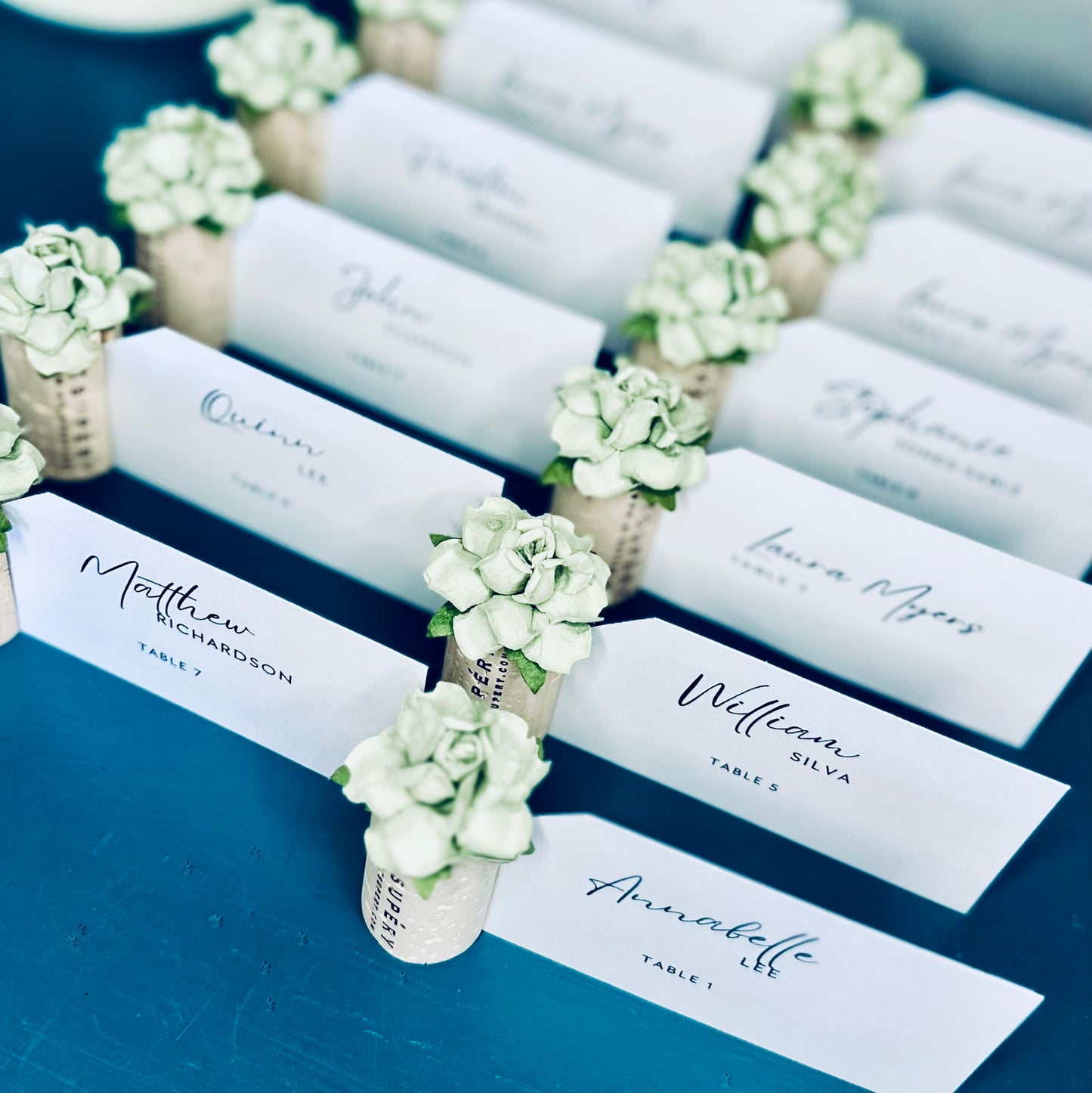 Place cards holders with succulent-style floral embellishments on a blue surface