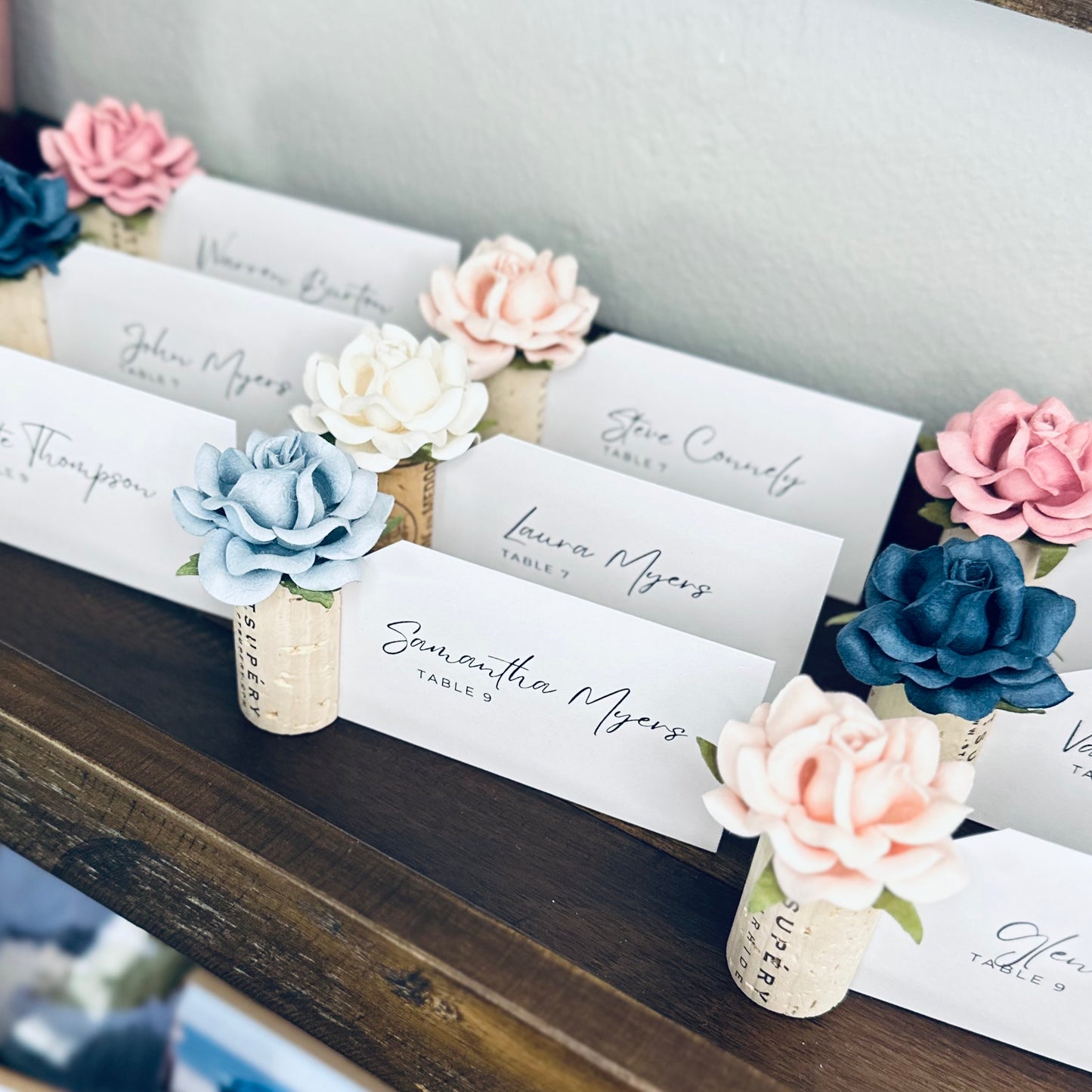 Place cards displayed in standing wine corks, with floral designs on a wooden surface