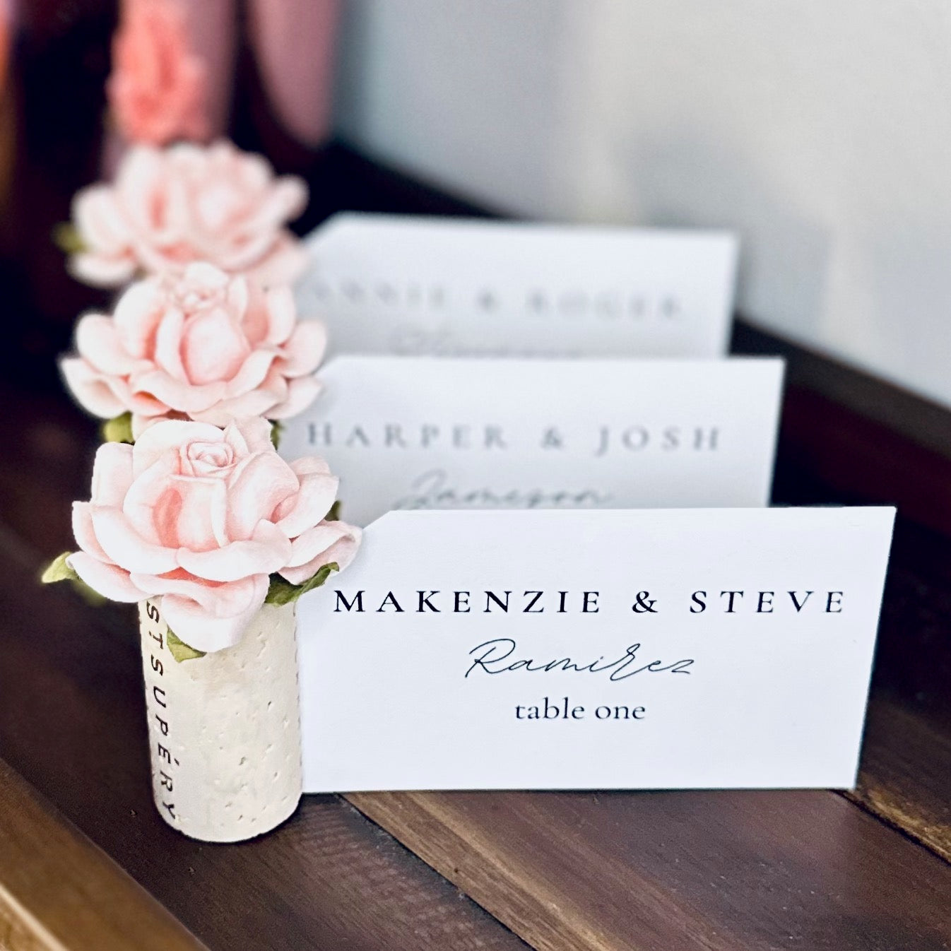 Wine cork place card holders with personalized name cards, displayed on a rustic, wooden shelf.