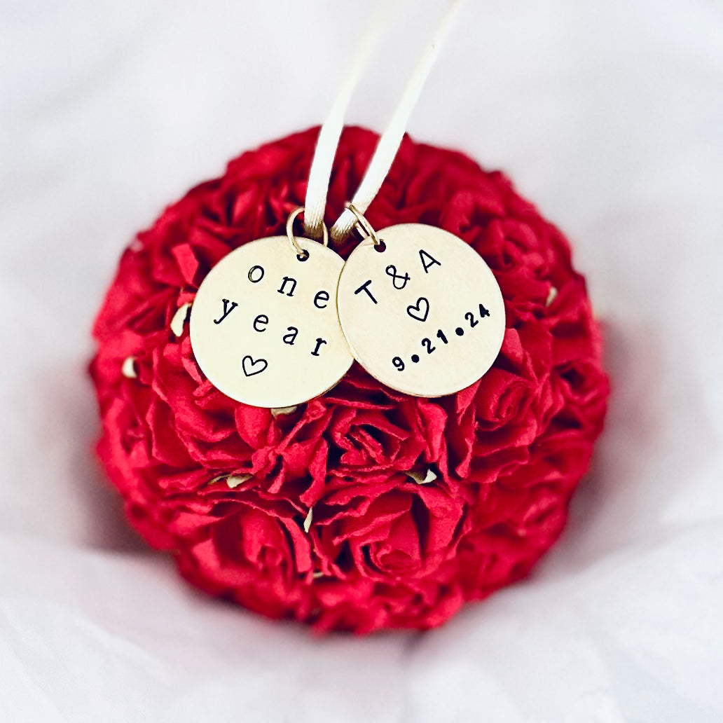 a red paper flower ball ornament with two custom charms. One charm reads "one year" for a 1st anniversary paper theme gift. The other charm is a couples' initials and wedding date.