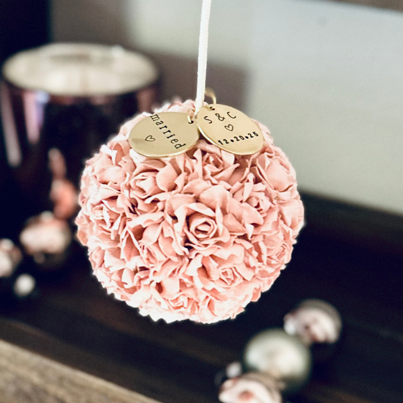 Pink floral wedding ornament with personalized gold charms on a blurred background