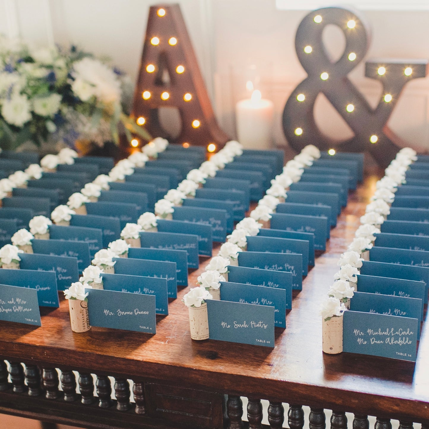 a wedding place card table displays guest name cards and seating assignments. The place cards are held by wine cork place card holders, with white succulent style flowers on top.