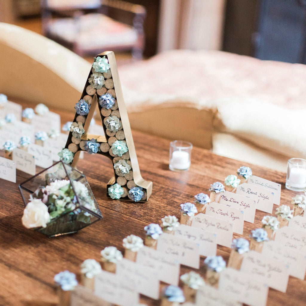 a wedding place card table with cornflower blue and mint green succulent flower place card holders. The holders display guest names and table assignments on white name cards.
