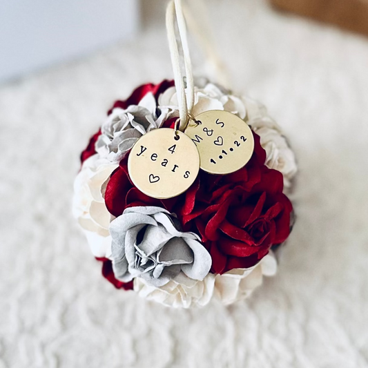Floral 4th wedding anniversary ornament with red, burgundy, white, and gray flowers and personalized gold charms on an ivory lace surface.
