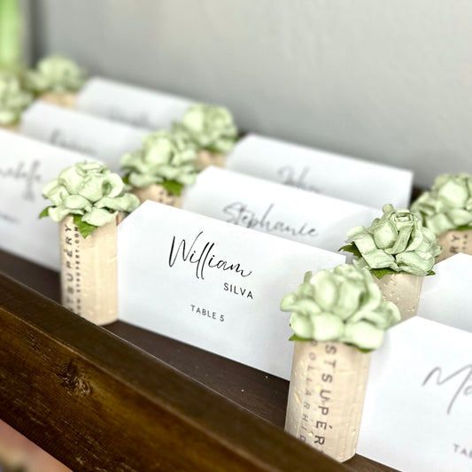 wedding reception seating cards displayed in wine cork place card holders with succulent-style flowers on top of the corks.  Suggests a garden or southwest theme wedding.