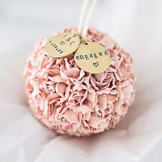 Pink flower engagement ornament with 'engaged' charm on a white tissue background