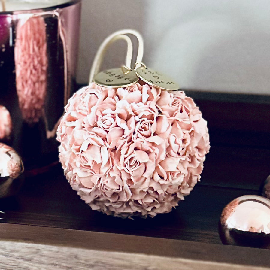 Blush pink floral engagement ornament with personalized charms, displayed on a wooden surface