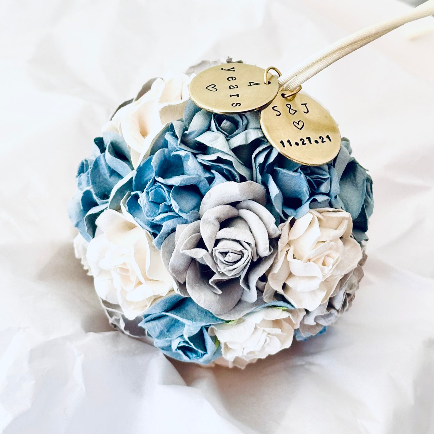 4th anniversary flower theme ornament with blue, gray, and white flowers and personalized gold charms on a white tissue background.