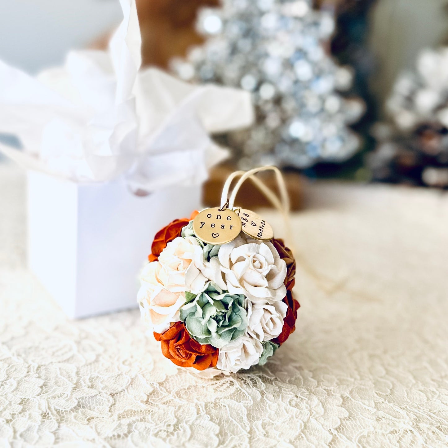 a 4th anniversary flower theme ornament gift in shades of white, ivory, sage, and terra cotta.  The ornament rests on an ivory lace surface, with a glossy white gift box in the background.