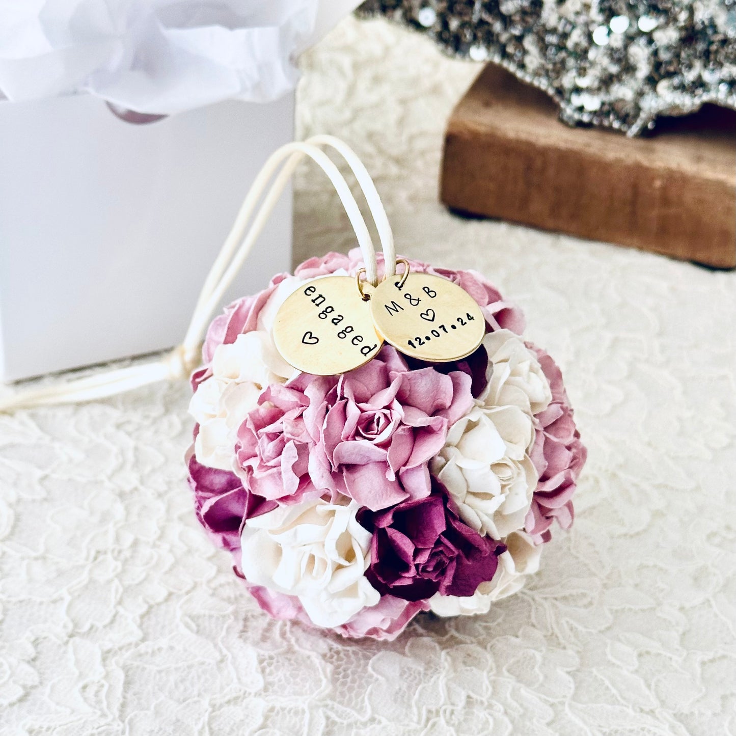 Personalized floral engagement ornament with 'engaged' charm, displayed on a textured surface.