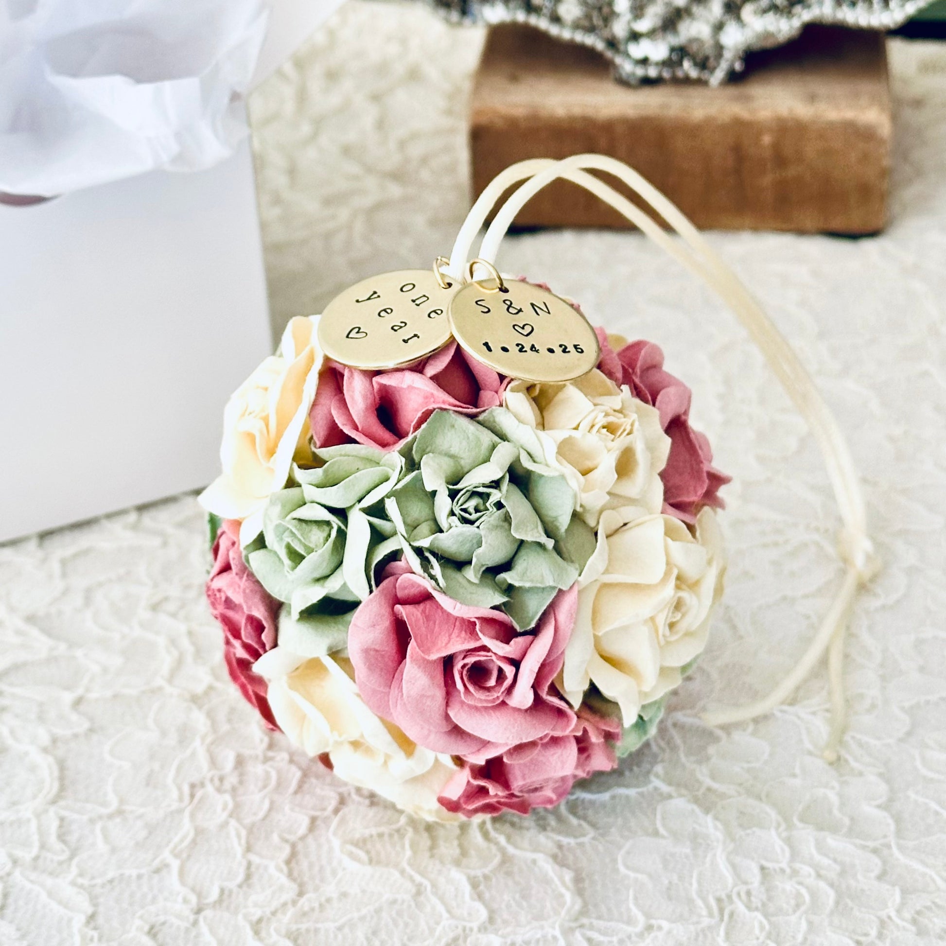Flower ball ornament celebrating a couples' one year anniversary on a lace surface.  Suggests an elegant anniversary keepsake gift.  The flowers are in shades of cream, sage, and mauve.