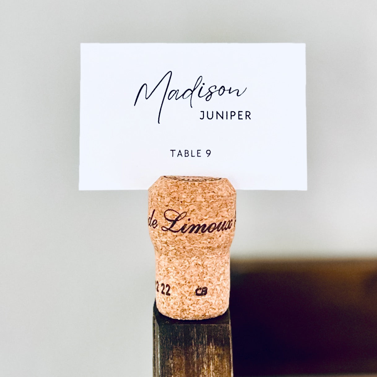 Champagne cork name card holder displaying guest name 'Madison Juniper' on a white name card.