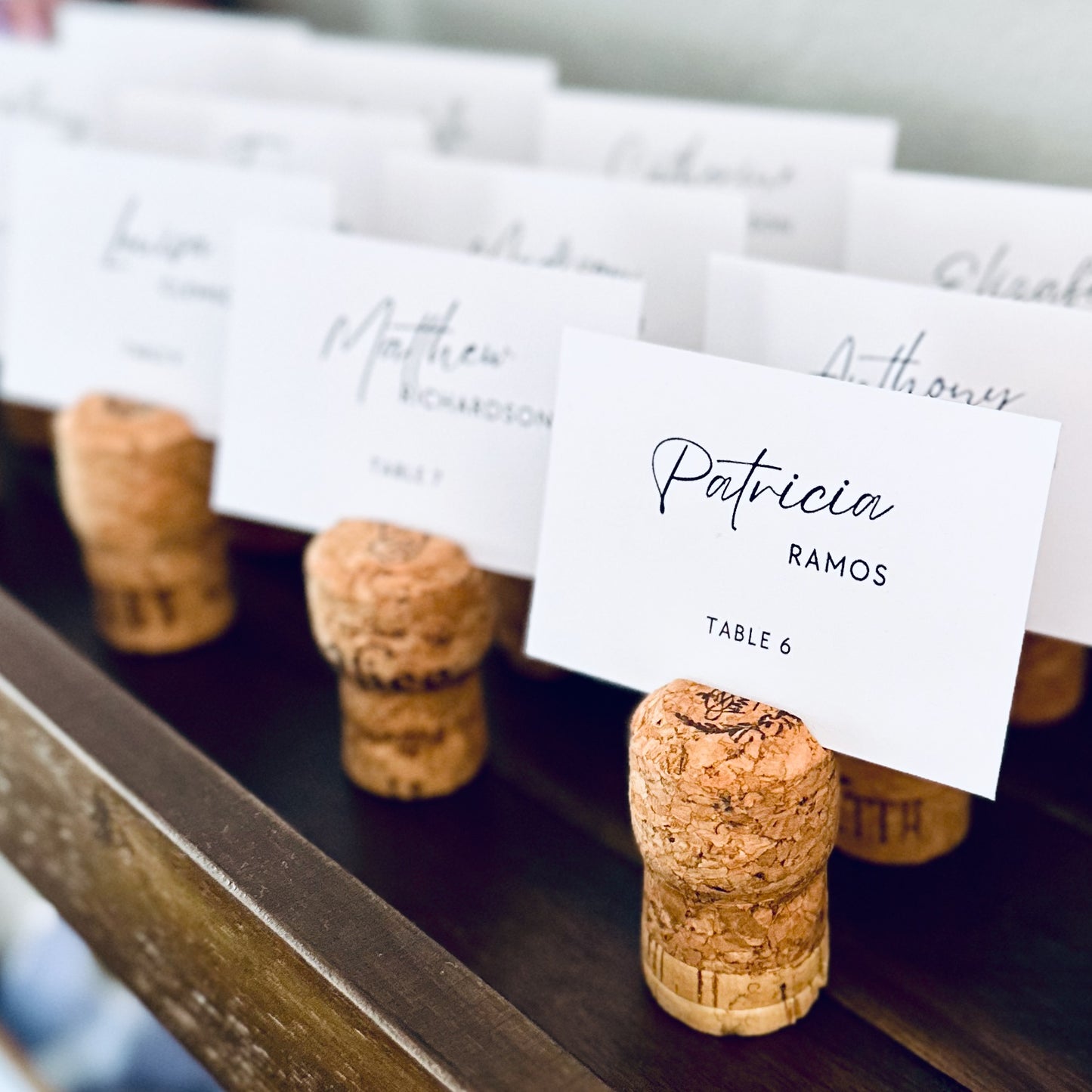 champagne cork escort card holders with printed guest name cards displayed on a rustic wooden shelf.
