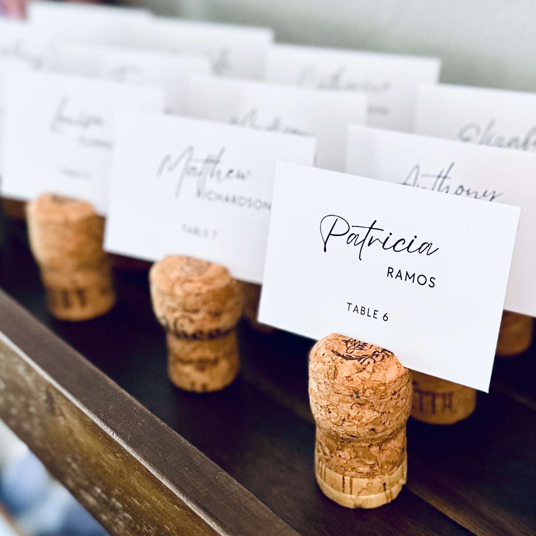 champagne cork escort card holders with printed guest name cards displayed on a rustic wooden shelf.