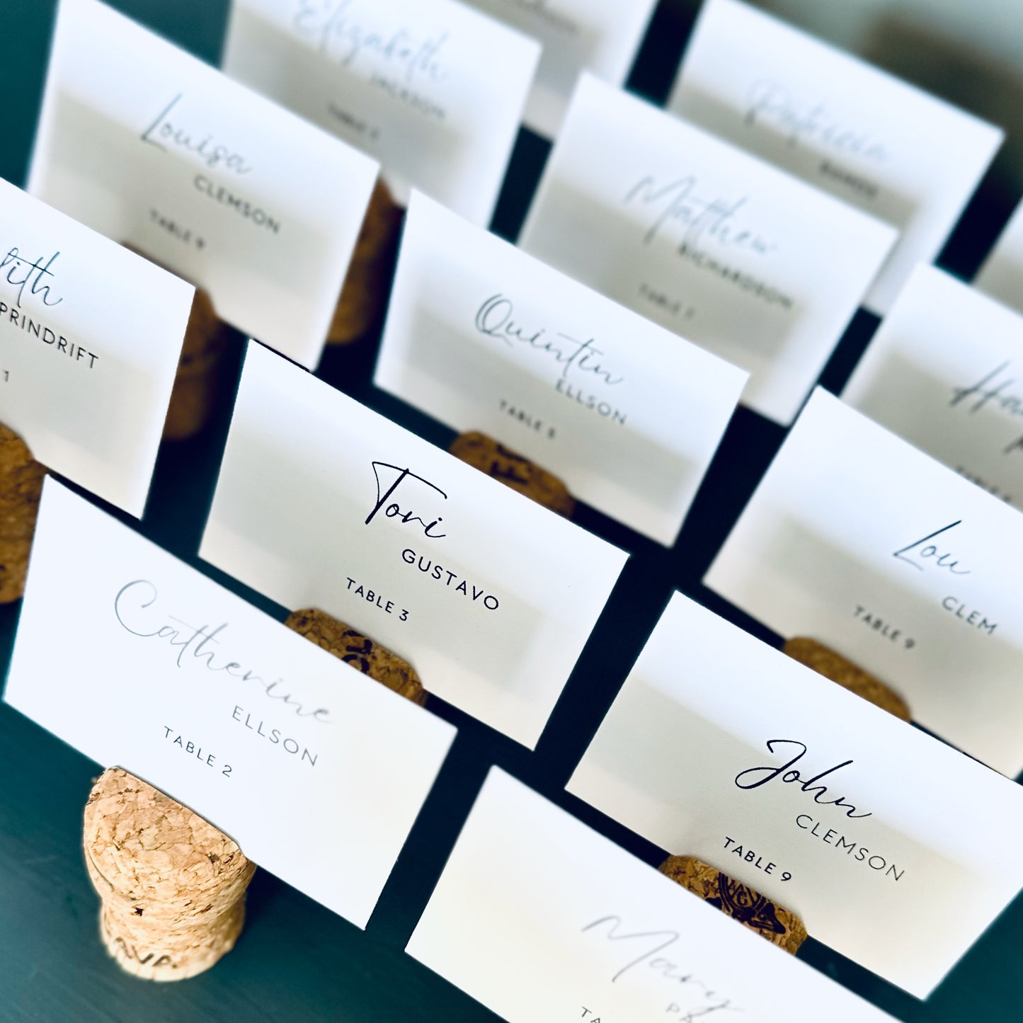 Set of personalized wedding guest name cards displayed in champagne cork place card holders, on a blue wooden surface.