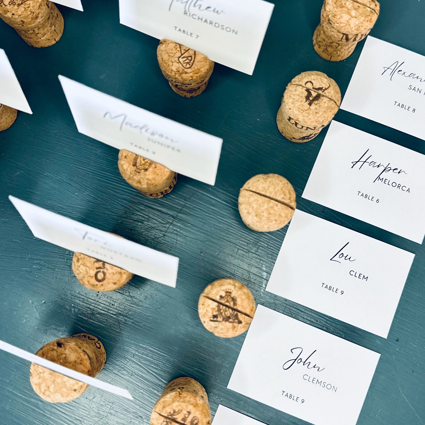 Champagne cork place card holders with printed guest name cards, on a teal surface