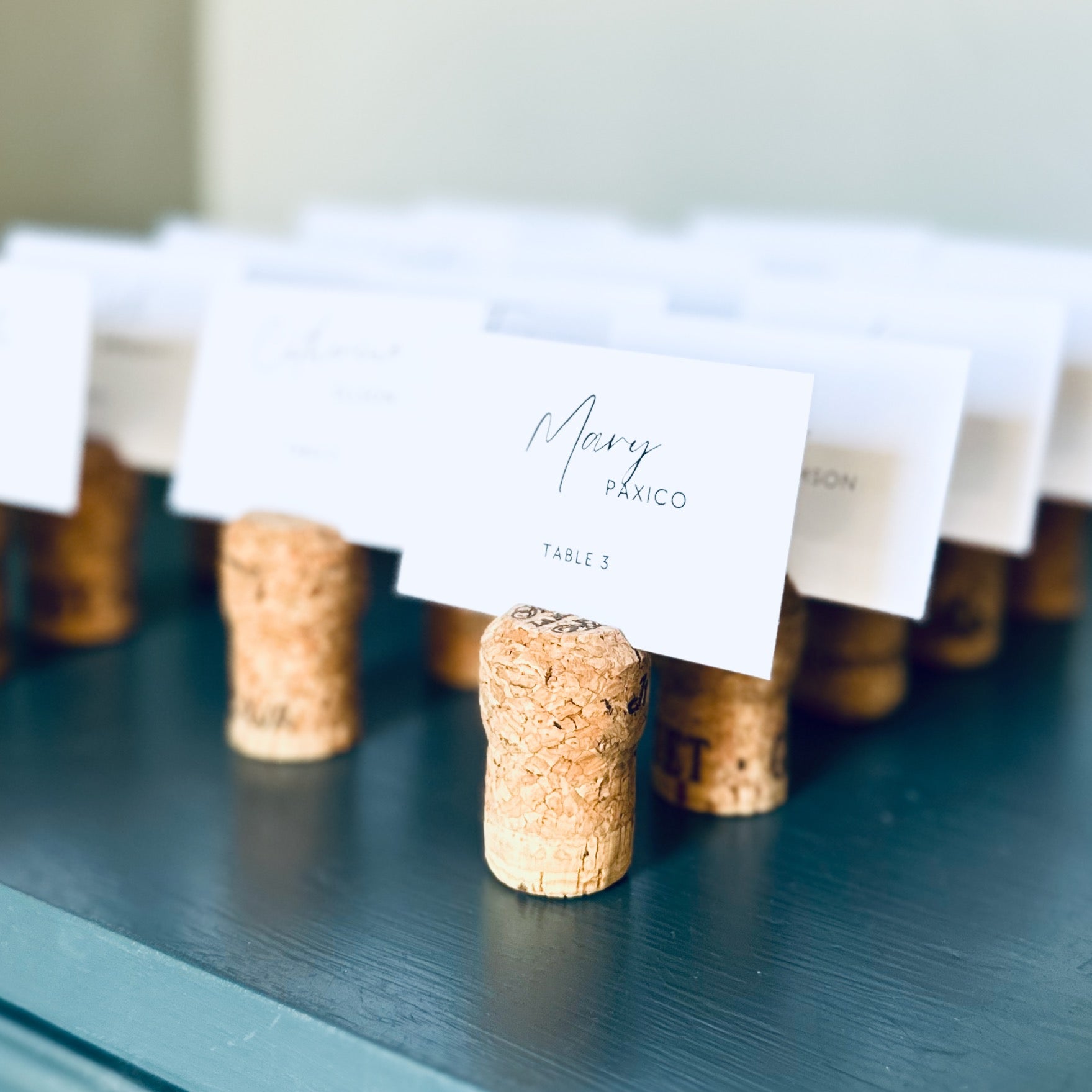 champagne cork place card holders with name cards, displayed on a dark surface.  Suggests a winery wedding celebration.