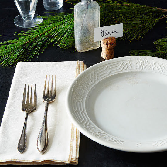 a holiday table place setting with greenery decor.  A champagne cork place card holder displays guest name "Oliver" on a printed white name card.